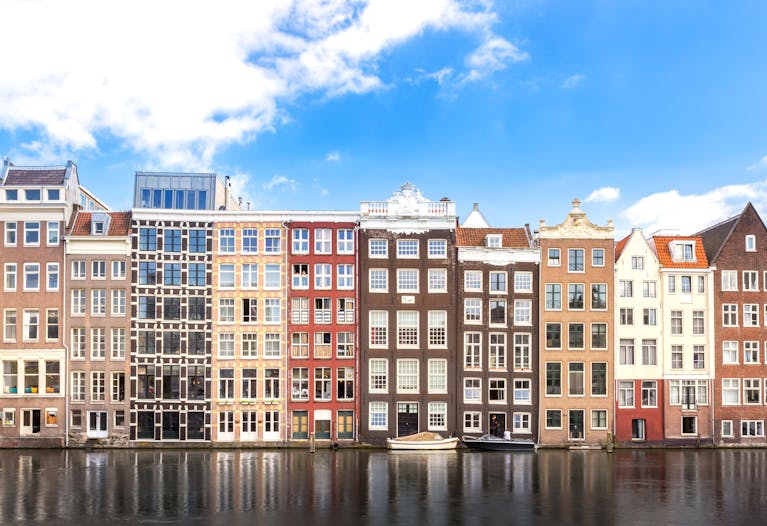 Colorful Amsterdam canal houses reflecting on water under a bright sky.