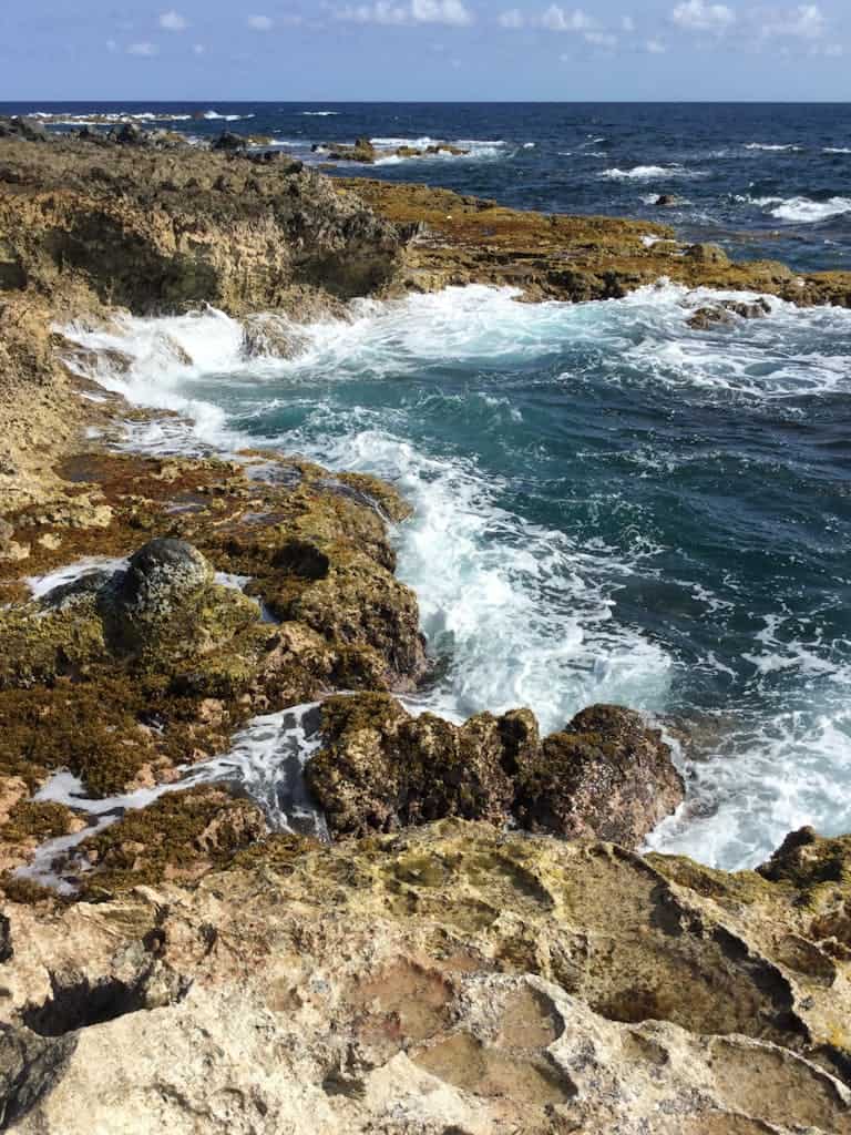 Crashing waves against rocky coastline in Oranjestad, Aruba on a sunny day.