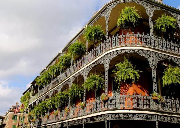 Detailed view of ornate ironwork balconies with lush greenery in New Orleans under a vibrant sky.